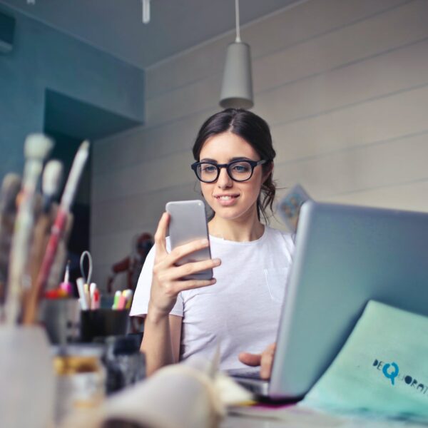 woman in white t shirt holding smartphone in front of laptop